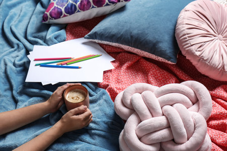 Woman holding cup of coffee while lying on bed with pillows and warm plaid, closeupの写真素材