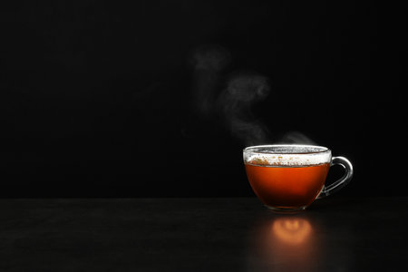 Glass cup of hot tea on table against black background, space for textの写真素材