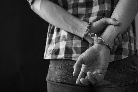 Criminal detained in handcuffs against dark background, space for text. black and white effectの写真素材