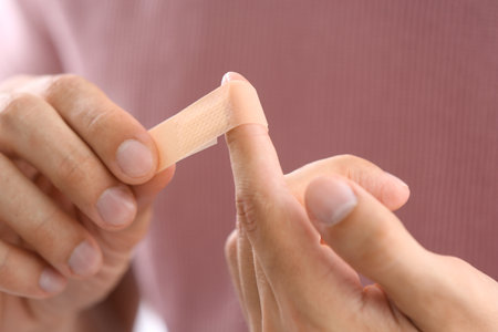 Man applying adhesive bandage on finger, closeup viewの写真素材