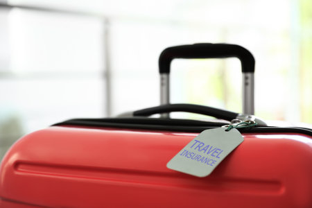 Stylish suitcase with travel insurance label on blurred background, closeupの写真素材