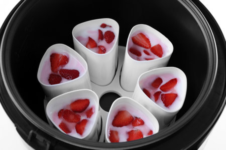 Cups of homemade strawberry yogurt in modern multi cooker on white backgroundの写真素材