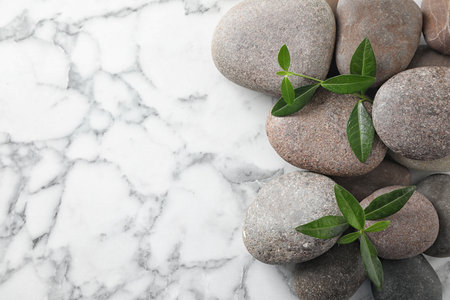 Spa stones and green leaves on marble table, flat lay with space for textの写真素材