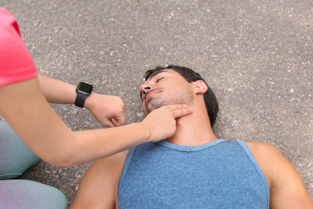 Young woman checking pulse of unconscious man on streetの写真素材