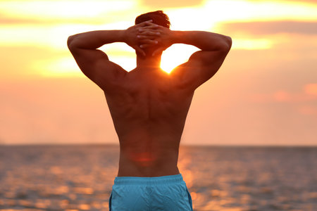 Handsome young man posing on beach near sea at sunsetの写真素材
