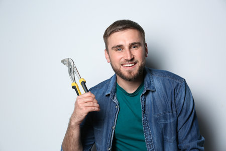 Young working man with adjustable pliers on light background