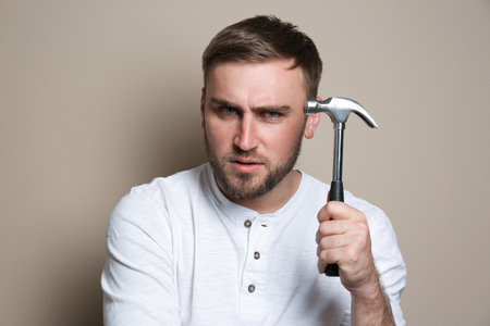 Young working man with hammer on beige backgroundの写真素材