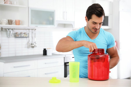 Young athletic man preparing protein shake in kitchen, space for textの写真素材