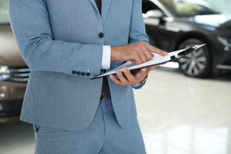 Young salesman with clipboard in modern car dealership, closeupの写真素材
