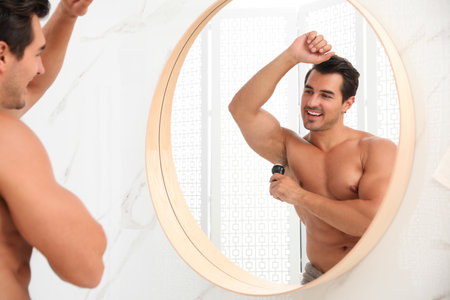 Handsome young man applying deodorant in bathroomの写真素材