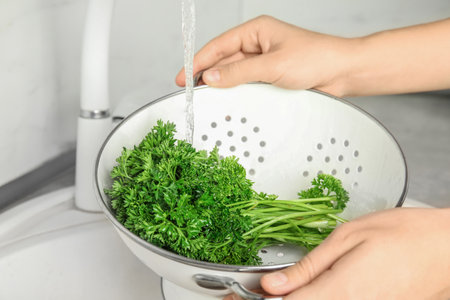 Woman washing fresh parsley in colander under tap water, closeupの写真素材