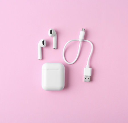 Modern wireless earphones and charging case with cable on pink background, flat layの写真素材