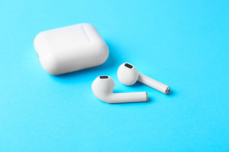 Modern wireless earphones and charging case on light blue background
