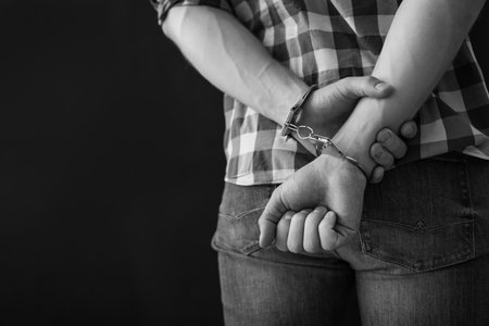 Criminal detained in handcuffs against dark background, space for text. black and white effectの写真素材