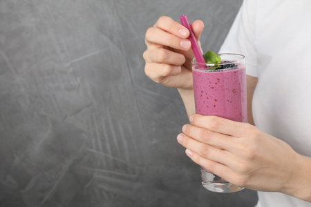 Young woman holding glass of tasty blackberry smoothie on gray background, closeup. Space for textの写真素材