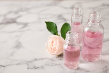 Bottles of essential oil and rose on marble table. Space for textの写真素材