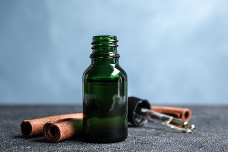 Bottle of essential oil and cinnamon sticks on table against blue backgroundの写真素材