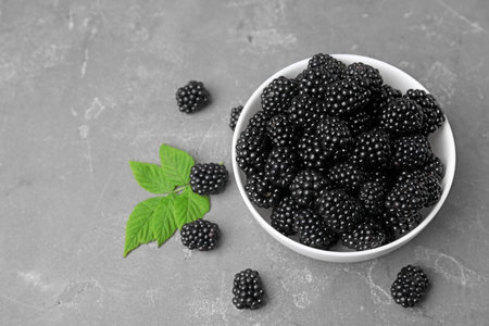 Bowl with ripe blackberries and leaves on gray table
