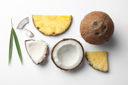 Composition with coconuts, juicy and leaves pineapple slices on white background, top view