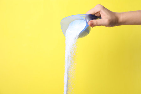 Woman pouring laundry powder from measuring cup on yellow background, closeupの写真素材