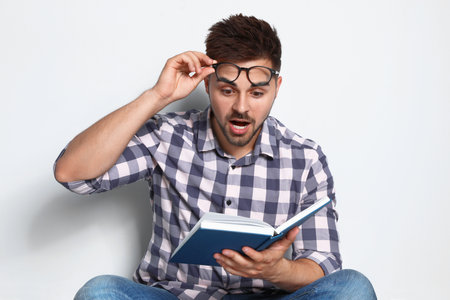 Handsome young man reading book on light backgroundの写真素材
