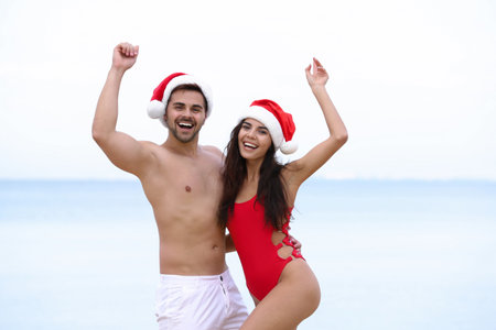 Happy young couple with Santa hats together on the beachの写真素材