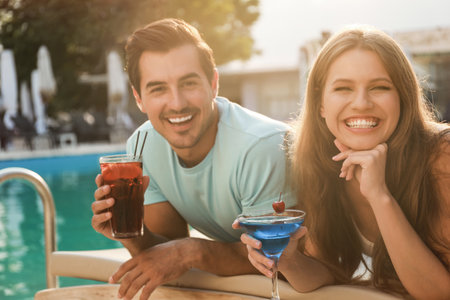 Happy young couple with fresh summer cocktail relaxing near swimming pool