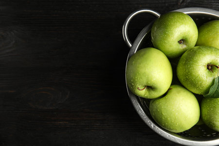 Colander of fresh ripe green apples on black wooden table, top view. Space for textの写真素材