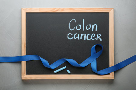 Chalkboard with blue awareness ribbon and words COLON CANCER on gray background, top view. Space for textの写真素材