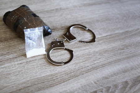 Drugs with handcuffs on wooden background, space for text. criminal lawの写真素材