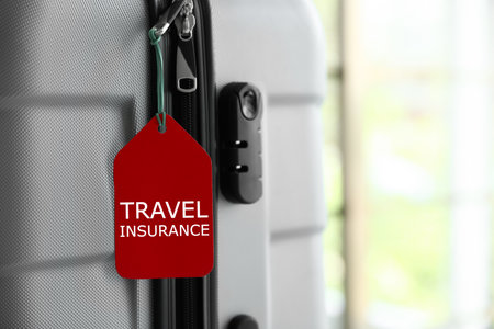 Stylish suitcase with travel insurance label on blurred background, closeup. Space for textの写真素材