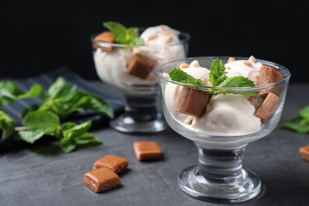 Glass bowls of ice cream with caramel candies and mint on gray tableの写真素材