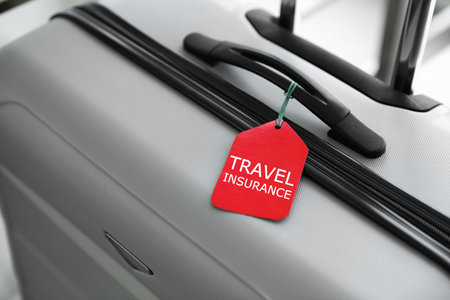 Stylish suitcase with travel insurance label on blurred background, closeup. Space for textの写真素材