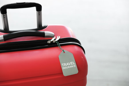 Stylish suitcase with travel insurance label on light background, closeup. Space for textの写真素材