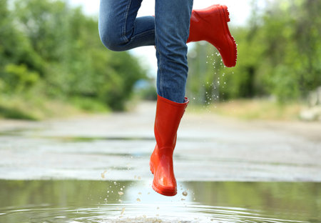 Woman with red rubber boots jumping in puddle, closeup. rainy weatherの写真素材