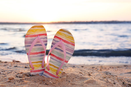Stylish flip flops on sand near sea, space for text. beach accessoriesの写真素材