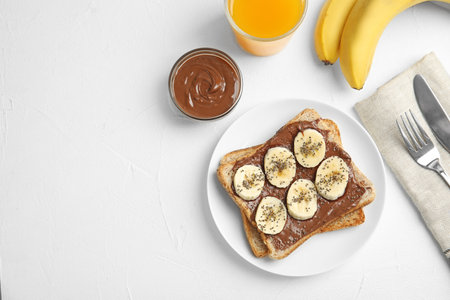 Slice of bread with chocolate paste and banana on white table, flat lay. Space for textの写真素材