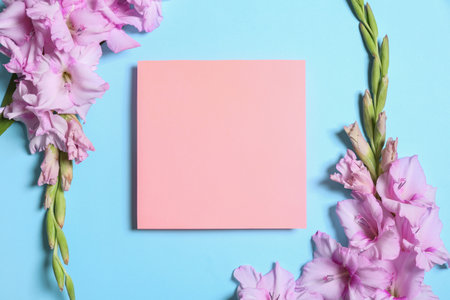 Beautiful gladiolus flowers with blank card on blue background, flat lay. Space for textの写真素材