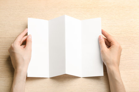 Young woman holding blank brochure at light wooden table, top view. Mock up designの写真素材