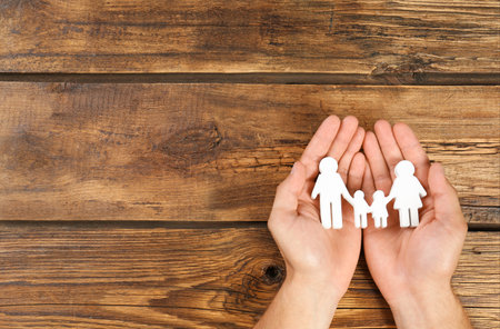 Young man holding family figure in his hands against wooden background, top view. Space for textの写真素材
