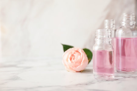 Bottles of essential oil and rose on marble table. Space for textの写真素材