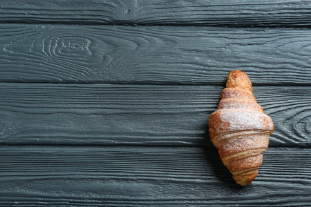 Tasty croissant with powdered sugar and space for text on dark wooden background, top view. french pastryの写真素材