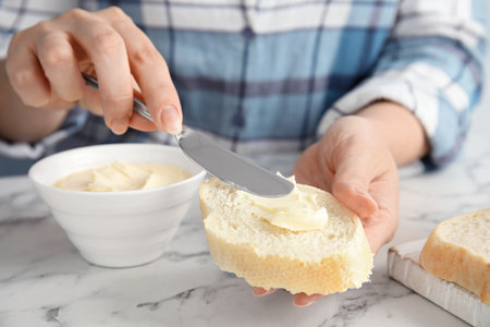 Woman spreading butter onto slice of bread over marble table, closeupの写真素材