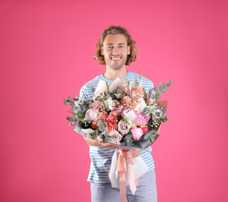 Young handsome man with beautiful flower bouquet on pink backgroundの写真素材