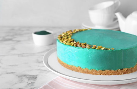 Delicious homemade spirulina cheesecake decorated with pistachios on marble table against light...