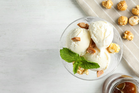 Delicious ice cream with caramel candies and popcorn in dessert bowl on white wooden table, flat lay. Space for textの写真素材