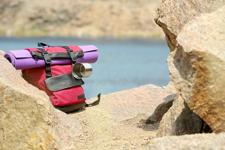 Camping backpack with mat and mug on stones near river. Space for textの写真素材