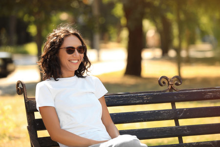 Happy young woman sitting on bench in parkの写真素材
