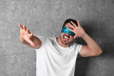 Young man wearing light blue blindfold on grey backgroundの写真素材
