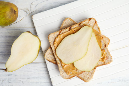 Slice of bread with peanut butter and pear on white wooden table, flat layの写真素材
